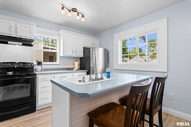 kitchen featuring black range with electric stovetop, under cabinet range hood, freestanding refrigerator, light wood-style floors, and backsplash