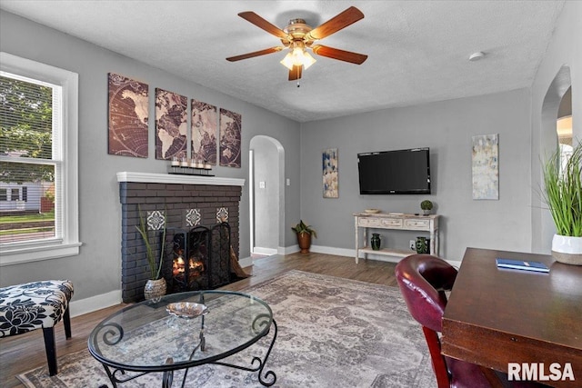 2557 S 6th St, Springfield, IL 62703 - living room featuring arched walkways, wood finished floors, a fireplace, ceiling fan, and a textured ceiling