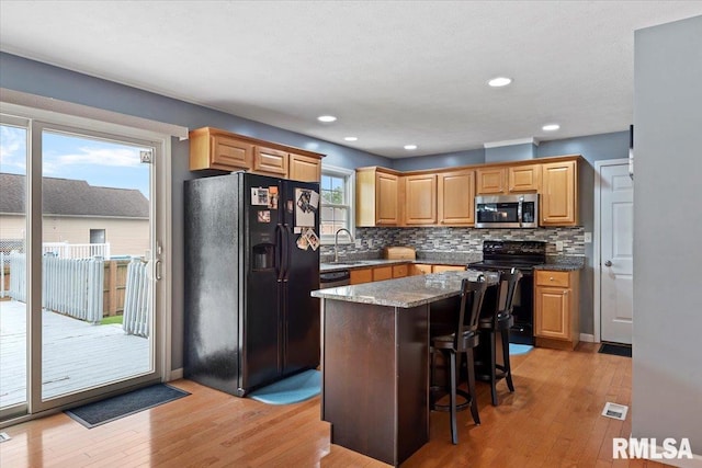 4108 Newtonmore Dr, Springfield, IL 62712 - kitchen with black appliances, light wood-style flooring, tasteful backsplash, a kitchen island, and a kitchen bar