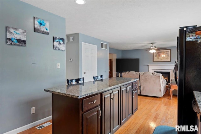 4108 Newtonmore Dr, Springfield, IL 62712 - kitchen featuring a ceiling fan, light wood-style floors, a warm lit fireplace, dark brown cabinets, and baseboards