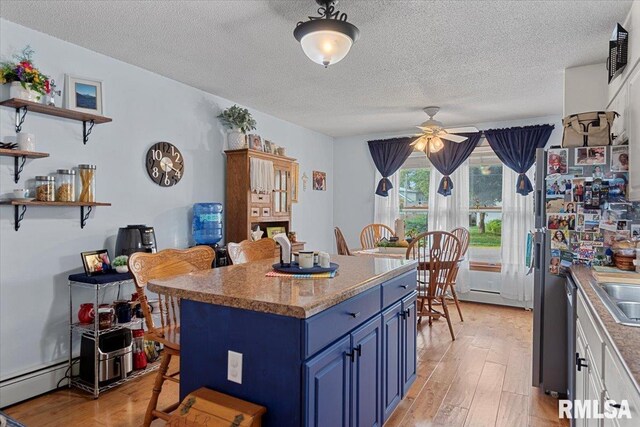 122 W Chapin St, Litchfield, IL 62056 - kitchen with blue cabinets, light wood-style floors, baseboard heating, a textured ceiling, and ceiling fan