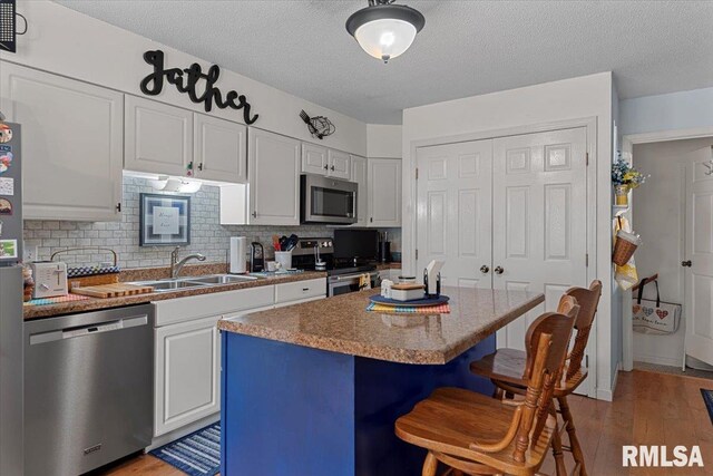 122 W Chapin St, Litchfield, IL 62056 - kitchen featuring appliances with stainless steel finishes, a sink, a kitchen bar, white cabinets, and light wood-style floors