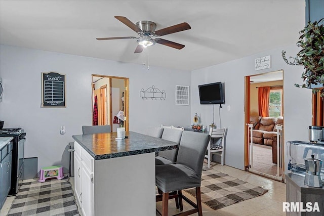 417 W Franklin St, Girard, IL 62640 - kitchen with gas stove, a ceiling fan, a kitchen breakfast bar, dark countertops, and white cabinetry