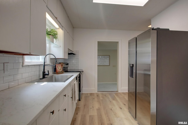 2204 Spring St, Quincy, IL 62301 - kitchen featuring appliances with stainless steel finishes, under cabinet range hood, white cabinetry, light wood-style flooring, and backsplash