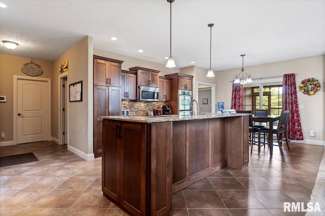 5408 Cromwell Pl, Springfield, IL 62711 - kitchen with stainless steel microwave, backsplash, an island with sink, light stone counters, and decorative light fixtures