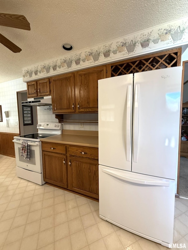 597 Walnut St, Knoxville, IL 61448 - kitchen with white appliances, under cabinet range hood, brown cabinetry, ceiling fan, and wallpapered walls