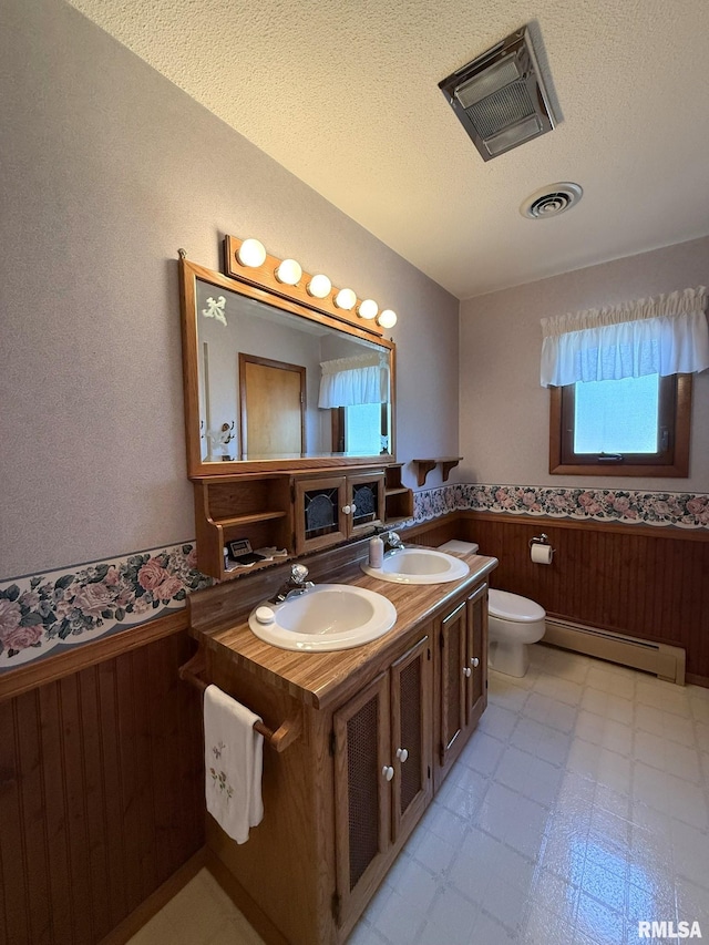 597 Walnut St, Knoxville, IL 61448 - bathroom featuring a baseboard heating unit, a wainscoted wall, a textured ceiling, double vanity, and wooden walls