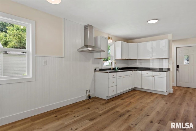 707 N Adams St, Lincoln, IL 62656 - kitchen featuring wall chimney range hood, light wood-style flooring, dark countertops, white cabinets, and wainscoting