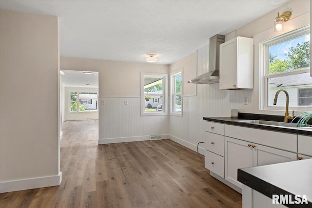 707 N Adams St, Lincoln, IL 62656 - kitchen featuring wall chimney exhaust hood, light wood-type flooring, plenty of natural light, wainscoting, and dark countertops