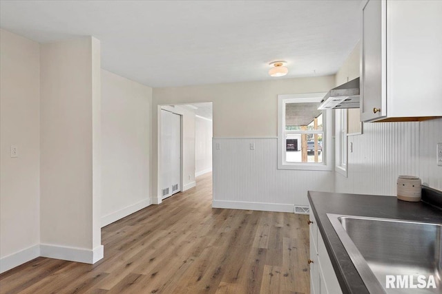 707 N Adams St, Lincoln, IL 62656 - kitchen featuring light wood finished floors, extractor fan, white cabinetry, a wainscoted wall, and dark countertops