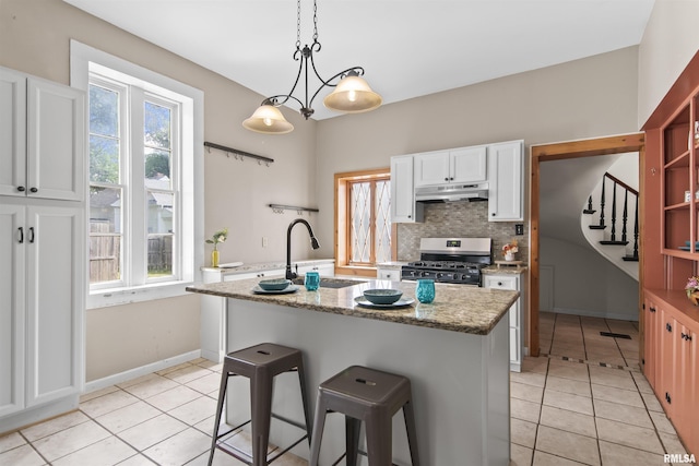 508 N Washington St, Mount Pulaski, IL 62548 - kitchen featuring stainless steel range with gas stovetop, under cabinet range hood, light tile patterned flooring, and white cabinets