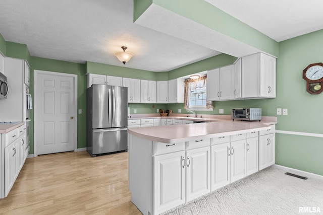 1860 Mayfield Rd, Chatham, IL 62629 - kitchen featuring stainless steel appliances, a peninsula, white cabinets, light countertops, and light wood-style floors
