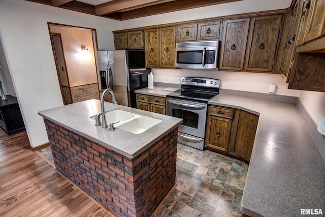 107 E Harrison St, Edinburg, IL 62531 - kitchen featuring appliances with stainless steel finishes, beamed ceiling, a center island with sink, and light countertops