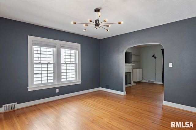 1829 S Walnut St, Springfield, IL 62704 - spare room featuring arched walkways, light wood-type flooring, a chandelier, and a fireplace with flush hearth