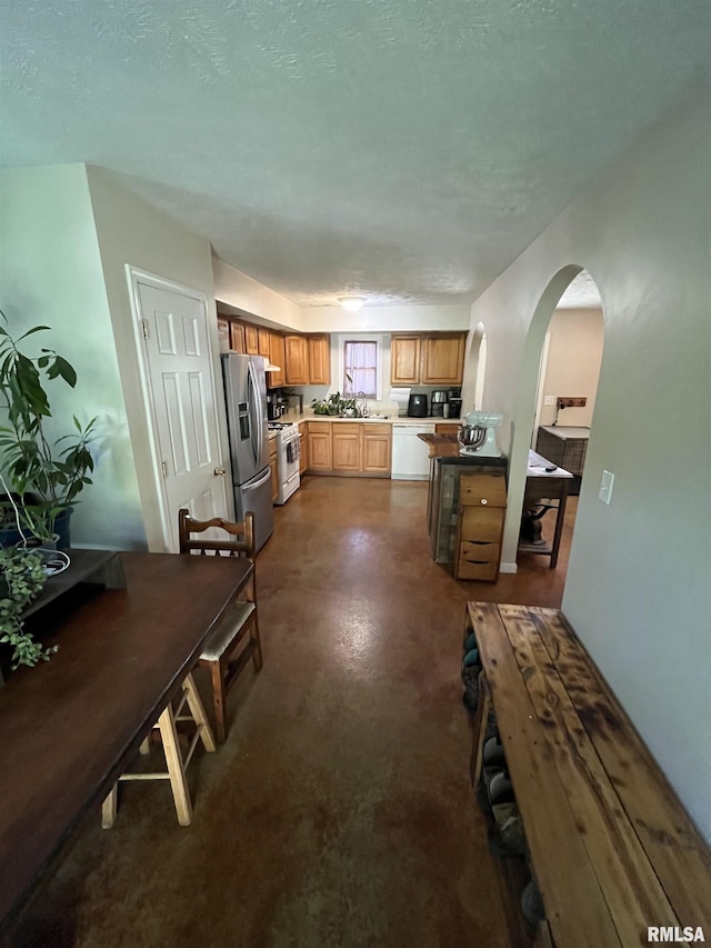 28 Albion St, Lynnville, IL 62650 - kitchen with white range with gas cooktop, arched walkways, stainless steel fridge, concrete floors, and brown cabinets