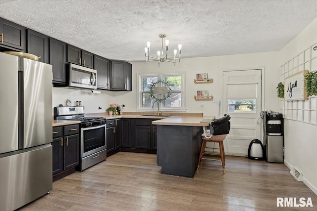 749 E Andrew Rd, Springfield, IL 62707 - kitchen with appliances with stainless steel finishes, a chandelier, light wood finished floors, a breakfast bar area, and a peninsula