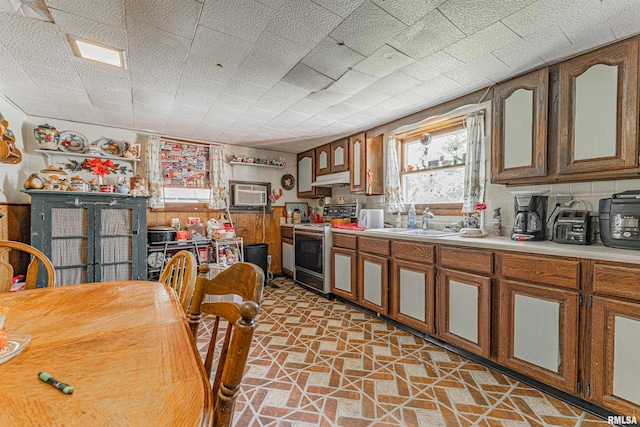 1214 Pekin St, Lincoln, IL 62656 - kitchen featuring white electric range oven, light countertops, under cabinet range hood, light stone finish floors, and brown cabinets
