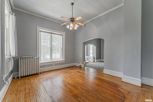 418 E Cooke St, Mount Pulaski, IL 62548 - empty room with radiator heating unit, ornamental molding, arched walkways, ceiling fan, and hardwood / wood-style floors