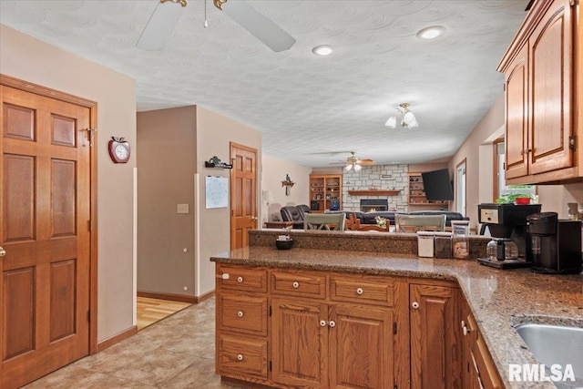 1420 Weston Pointe Dr, Springfield, IL 62704 - kitchen with a ceiling fan, a peninsula, brown cabinets, a fireplace, and dark stone countertops