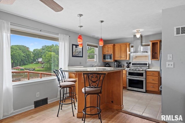 14 Beachview Ln, Springfield, IL 62712 - kitchen with appliances with stainless steel finishes, wall chimney range hood, a kitchen bar, brown cabinets, and hanging light fixtures