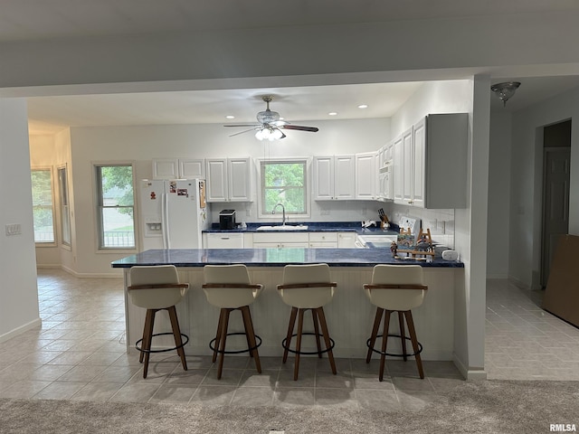 4004 Abbey Ridge St, Quincy, IL 62305 - kitchen featuring dark countertops, a peninsula, white appliances, white cabinetry, and a kitchen breakfast bar