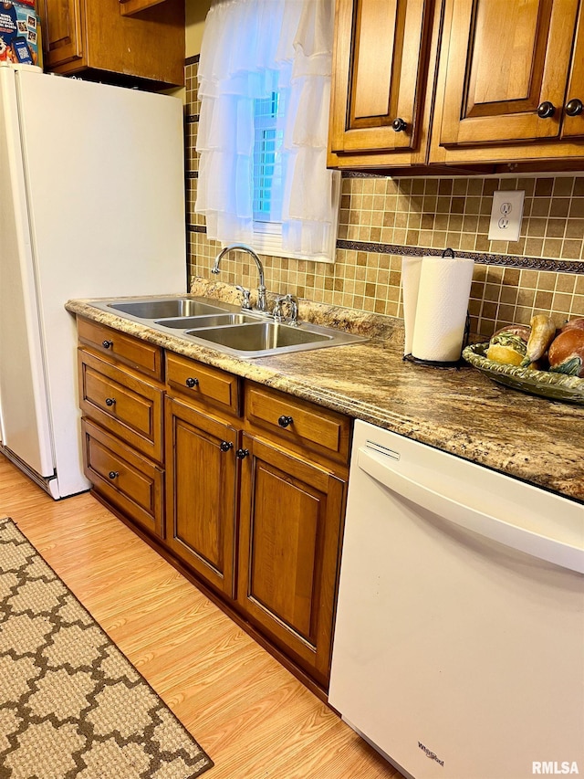 kitchen with light hardwood / wood-style floors, white appliances, stone counters, sink, and tasteful backsplash