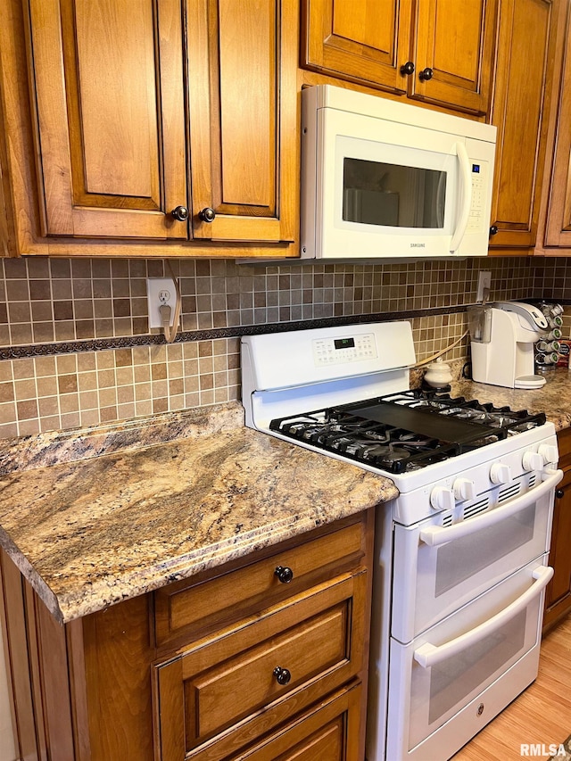 kitchen with white appliances, light stone countertops, tasteful backsplash, and light hardwood / wood-style floors