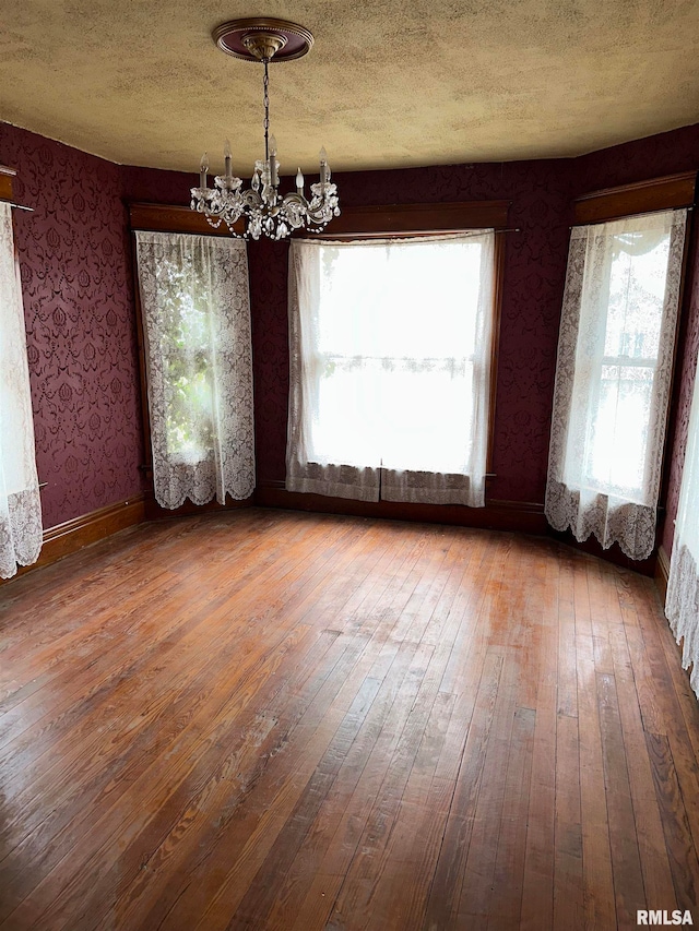 spare room featuring an inviting chandelier, a textured ceiling, and hardwood / wood-style floors