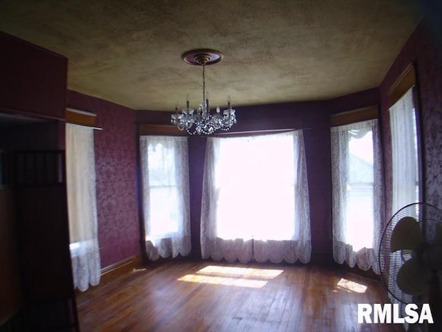 unfurnished dining area featuring a notable chandelier, plenty of natural light, and dark wood-type flooring