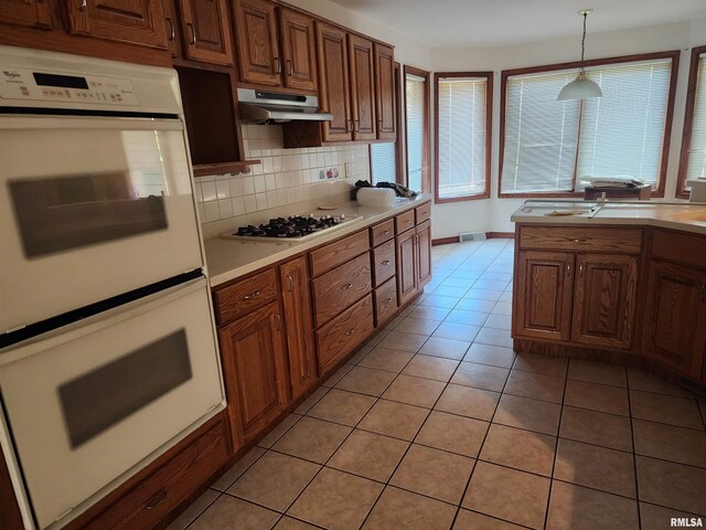 kitchen with hanging light fixtures, decorative backsplash, white appliances, and light tile patterned floors