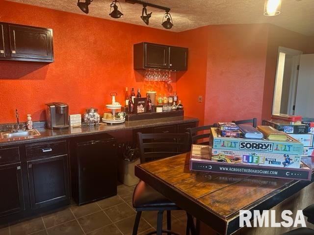 bar featuring dark brown cabinets, dishwasher, track lighting, dark tile flooring, and sink