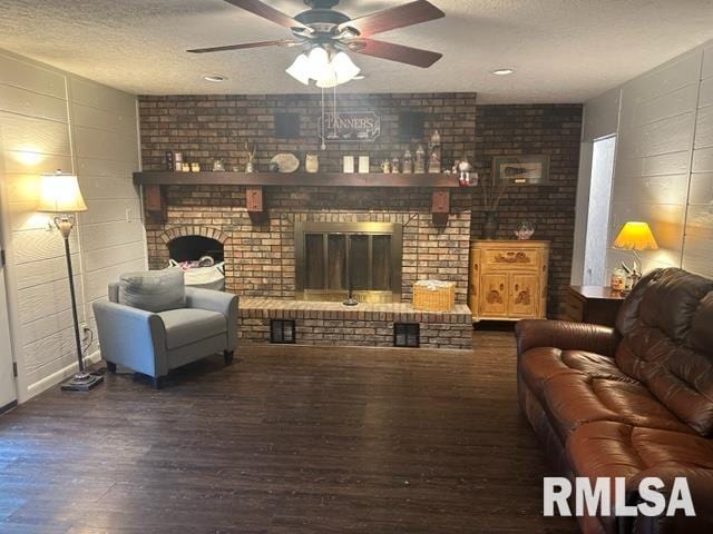 living room with ceiling fan, dark wood-type flooring, brick wall, and a brick fireplace