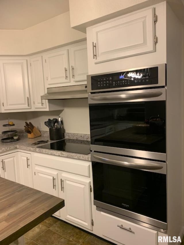 kitchen featuring black electric cooktop, double oven, dark tile flooring, and white cabinetry