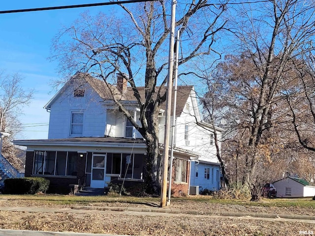 view of front of home featuring entry steps, central AC, brick siding, a sunroom, and a chimney