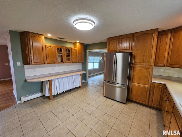 kitchen with a baseboard heating unit, decorative backsplash, stainless steel fridge, and light tile patterned flooring