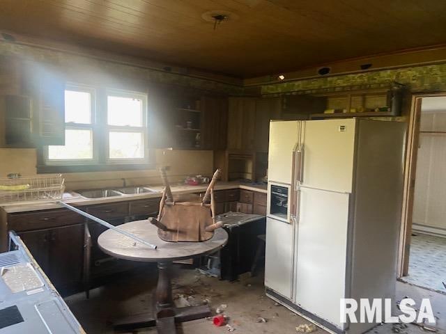 kitchen with wood ceiling, dark brown cabinetry, white refrigerator with ice dispenser, and sink