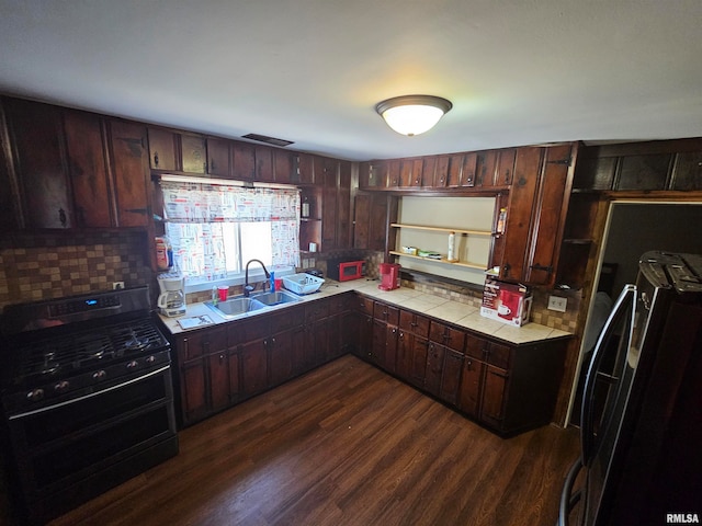 kitchen featuring gas stove, sink, dark brown cabinets, dark hardwood / wood-style flooring, and black fridge