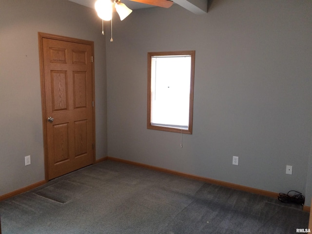 spare room featuring ceiling fan, dark carpet, and beamed ceiling
