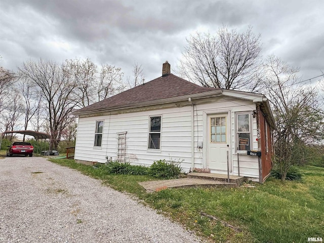 exterior space with gravel driveway, roof with shingles, a detached carport, and a chimney