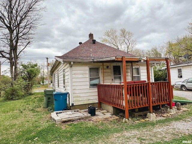 rear view of property featuring roof with shingles, a chimney, and a deck