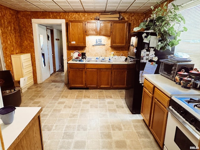 kitchen featuring freestanding refrigerator, white gas stove, a sink, light countertops, and brown cabinets