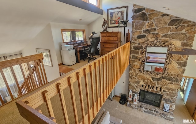 stairway featuring high vaulted ceiling, light carpet, and a stone fireplace