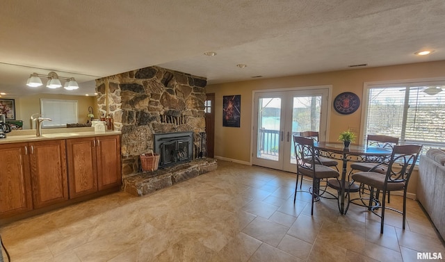 dining space featuring light tile floors, a stone fireplace, sink, a textured ceiling, and french doors