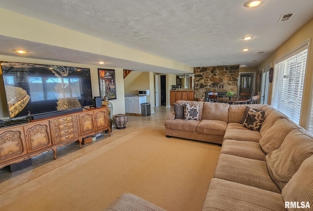 tiled living room with a textured ceiling and a stone fireplace