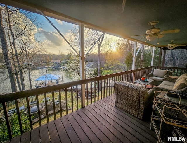 deck at dusk with a water view, ceiling fan, and an outdoor hangout area