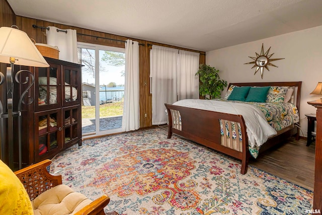 bedroom featuring access to exterior, wood walls, a textured ceiling, and hardwood / wood-style flooring