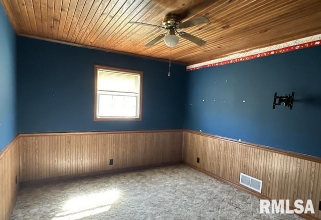 carpeted spare room with wood ceiling, wood walls, and ceiling fan