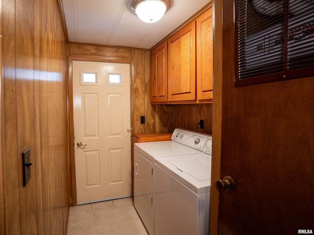 laundry area with cabinets, a textured ceiling, wooden walls, and separate washer and dryer