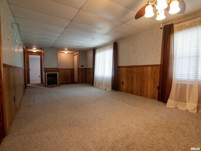 unfurnished living room with wood walls, carpet flooring, a drop ceiling, and a wealth of natural light