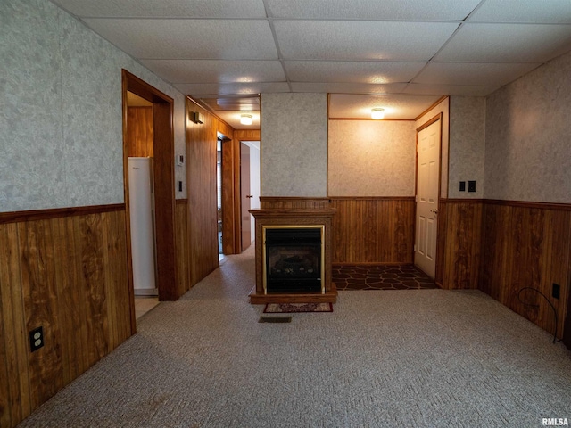 living room featuring a paneled ceiling, wooden walls, and carpet floors